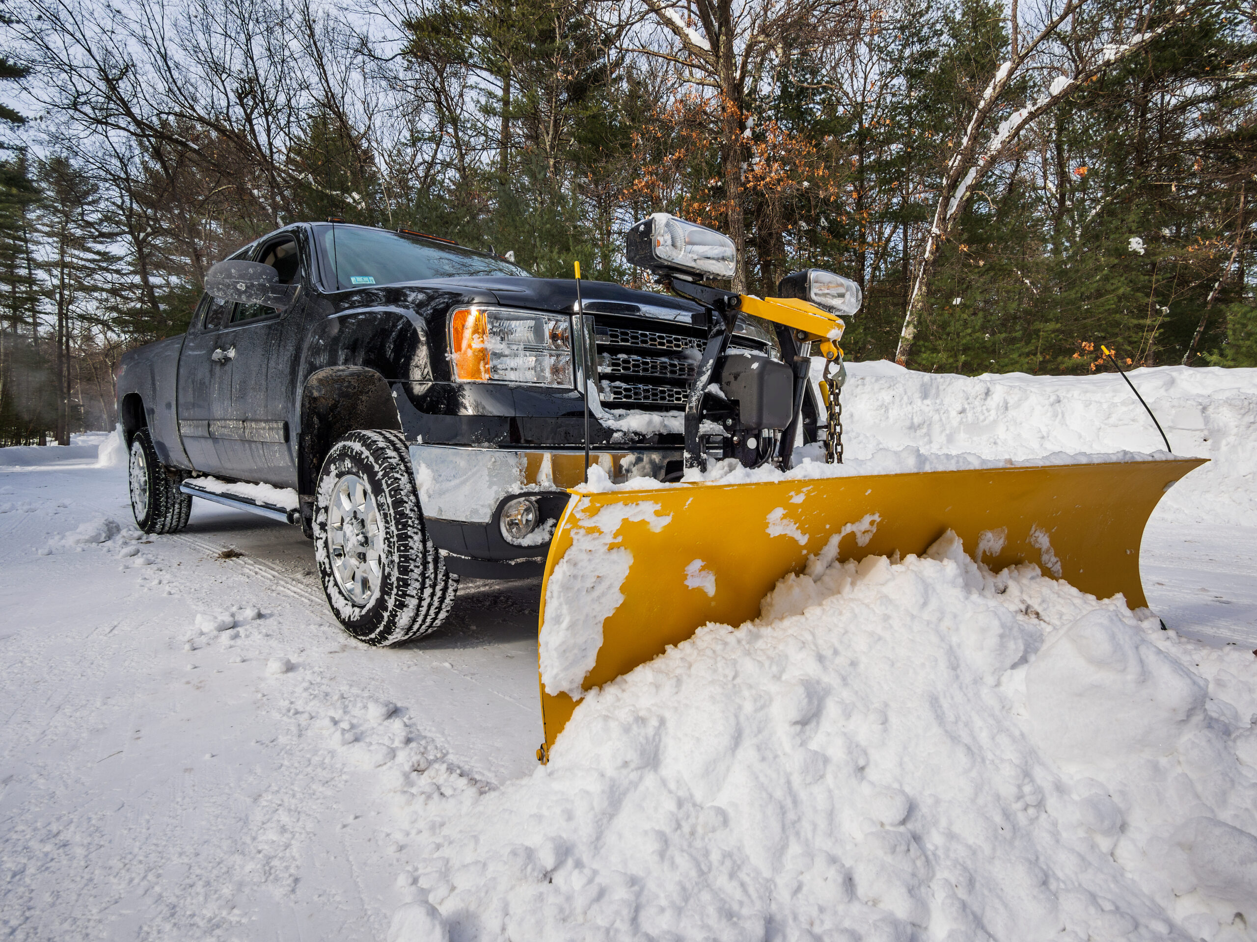 pickup truck with attached plow clearing driveway of snow